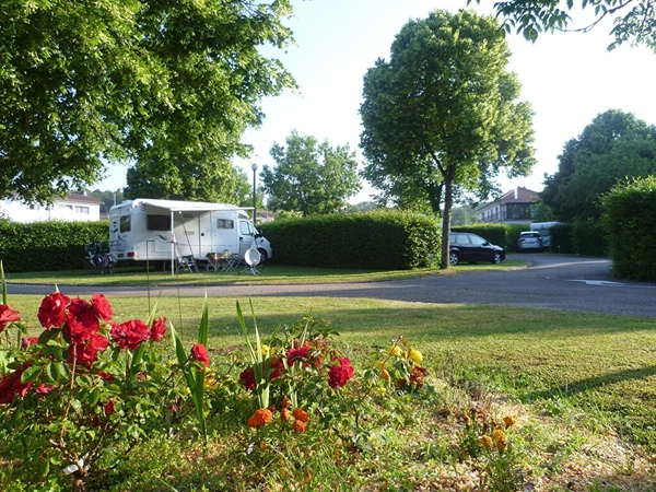 Camper parked under tree shade with chairs outside, amidst lush green surroundings and vibrant flower beds at Seasonova Vittel
