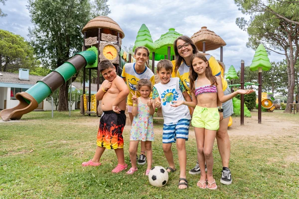 Group of smiling children and adults posing together in front of a colorful playground at Marina Julia Family Camping Village