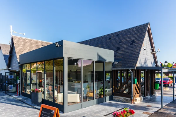 Modern reception building with glass walls and a wooden roof structure surrounded by cars and flower planters at Marvilla Parks La Vallée