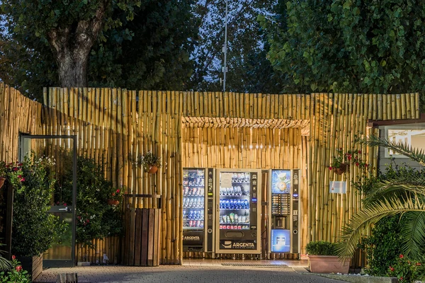 Vending machines dispensing snacks and drinks, enclosed by a lighted bamboo structure, surrounded by plants at hu Venezia Camping in Town