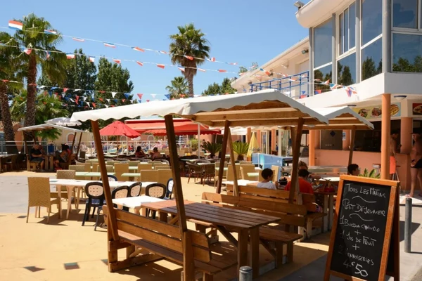 Wooden outdoor dining set, people seating, under sunshades, surrounded by other diners, bunting overhead at Marvilla Parks Club Le Napoléon