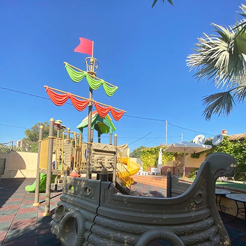 A pirate ship-shaped playground structure standing on a tiled area beneath a clear blue sky, surrounded by greenery at Armanello