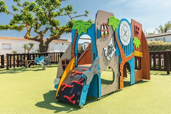 Colorful playground climbing structure resembling a pirate ship, situated in a fenced outdoor area with trees at Marvilla Parks Le Castellas