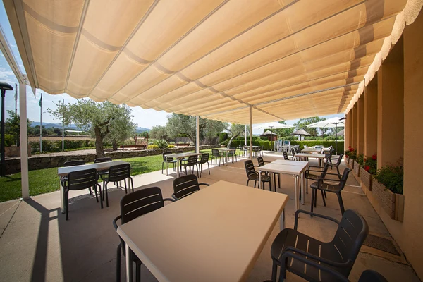 Tables and chairs sit under a large canopy on a patio overlooking a garden with trees and distant mountains at Els Ports