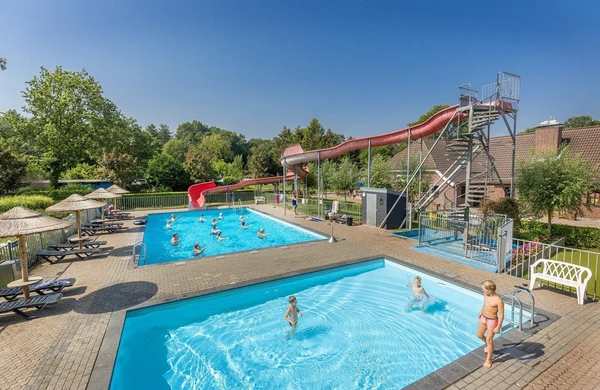 Swimming pools with people playing, surrounded by lounge chairs, umbrellas, and trees, featuring a tall waterslide at Hoeve de Schaaf