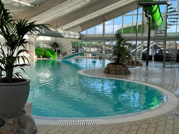 Indoor swimming pool with a spiraling waterslide, surrounded by potted plants and large windows at Dancamps Nordsø
