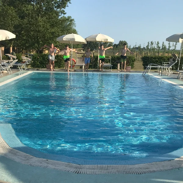 Five people about to jump into a swimming pool, surrounded by lounge chairs and umbrellas at Agriturismo Tenuta Regina