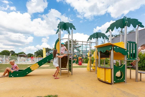Children play on colorful playground equipment featuring slides and climbing structures, set in an outdoor recreational area at Les 2 Fontaines