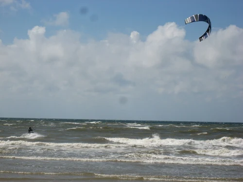 Kite surfer gliding over choppy waves under a partly cloudy sky at Dancamps Nordsø