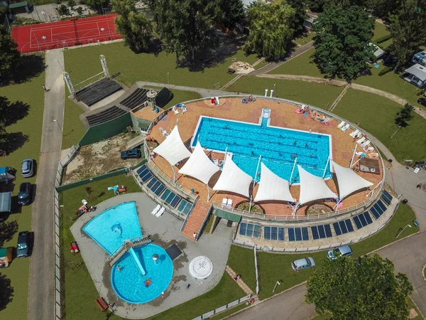 Aerial view of a large outdoor swimming pool with canopies, surrounded by a grassy area, smaller pool, and sports courts at Füred