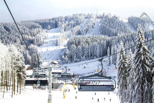 Ski lift transports people over snowy slopes and pine forests at a busy mountain ski resort at Bergresort Winterberg