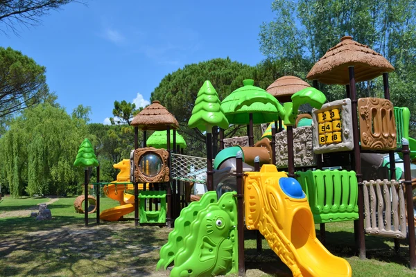 Colorful playground with slides and climbing structures, surrounded by lush green trees and grassy area at Marina Julia Family Camping Village