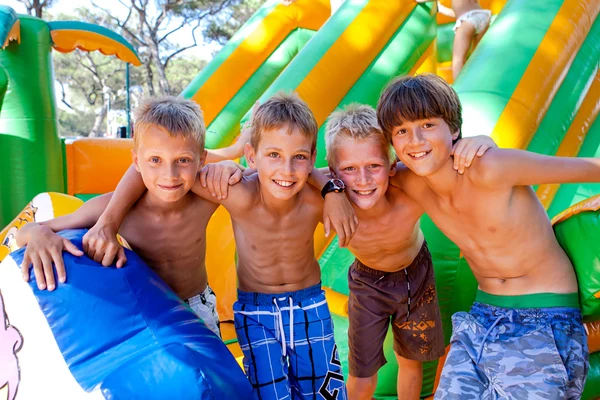 Four smiling boys with arms around each other stand in front of an inflatable slide, surrounded by greenery at El Pinar