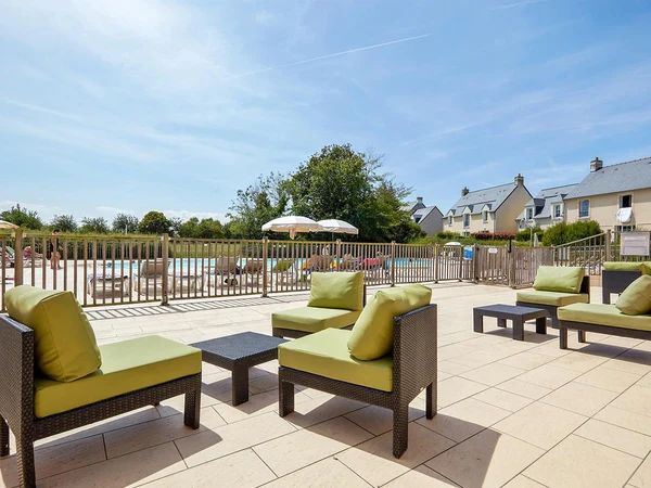 Outdoor lounge chairs facing a fence-enclosed pool area, surrounded by residential buildings and greenery at Le Green Beach