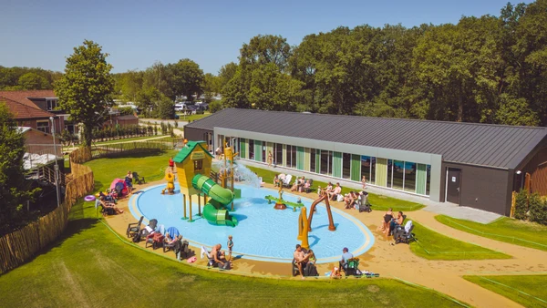 Children playing in a colorful splash pad featuring slides and sprinklers, surrounded by sunbathers and greenery at Marvilla Parks Kaatsheuvel