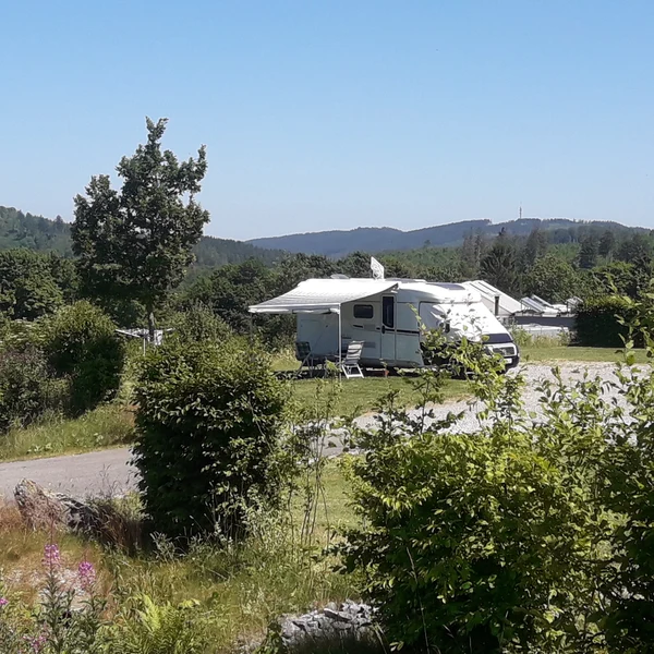 Camper van parked with awning extended and chairs set up nearby, surrounded by greenery and distant hills at Brilon