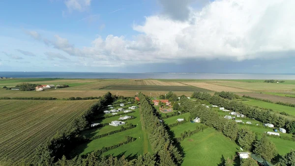 Caravans arranged in rows within a lush green campsite near fields and a distant coastline at Ballum
