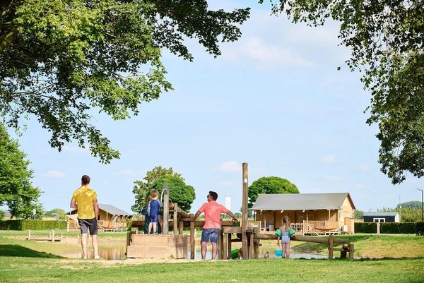People gathering around a wooden water play structure, surrounded by greenery and wooden cabins at Betuwe