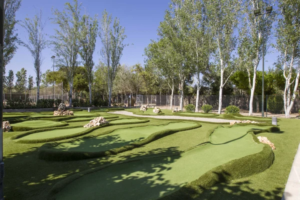 Miniature golf course with winding green paths among trees and shrubs, surrounded by a chain-link fence at Tamarit Beach Resort