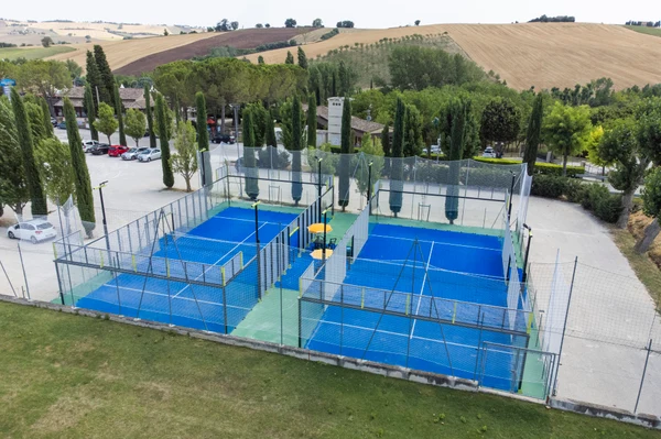 Padel courts are surrounded by a fence, located near parked cars and trees at a scenic campsite with rolling hills at Centro Vacanze Verde Azzurro