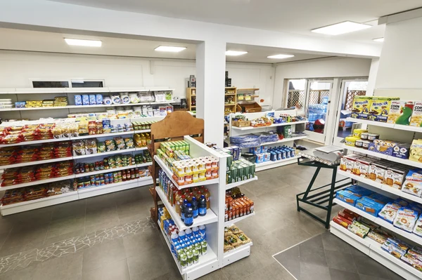 Shelves display various packaged foods and drinks in a brightly lit small grocery store at Porto Cesareo Camping