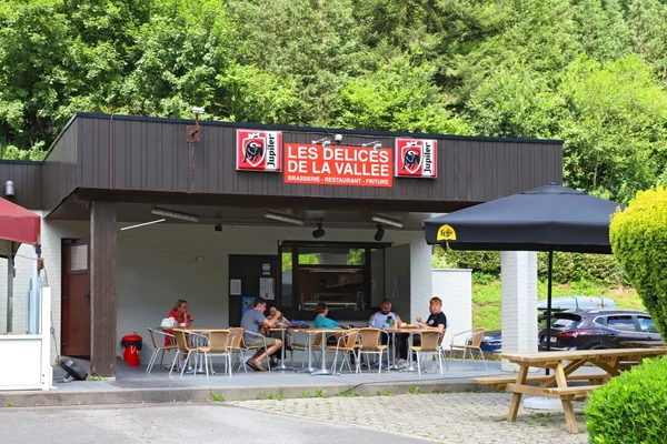 People sitting at outdoor café tables, eating and drinking, surrounded by greenery and cars at Floreal la Roche