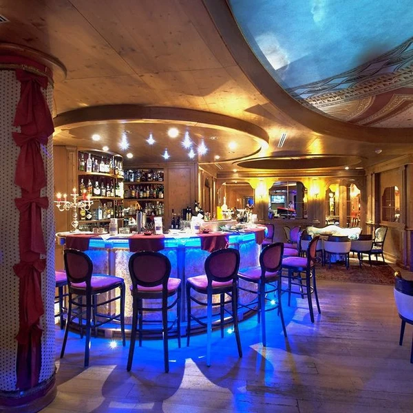 Circular bar with stools glows in blue light, surrounded by shelves of bottles in a warmly lit lounge at Cristal Palace Resort
