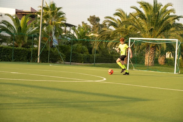 Child dribbling a soccer ball on a goal side court surrounded by palm trees at I Turchesi Club Village