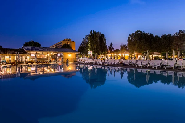 Swimming pool reflecting nearby buildings and trees at dusk, surrounded by many empty lounge chairs at hu Venezia Camping in Town