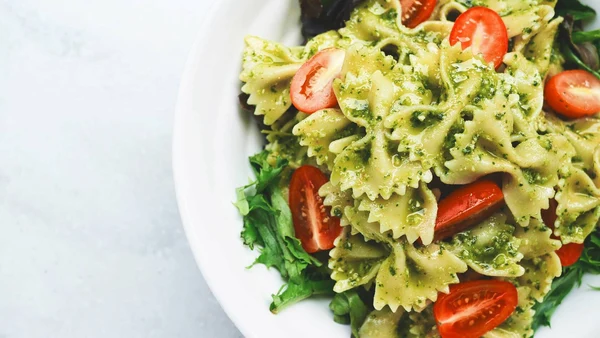 Bowl of pasta with pesto sauce and cherry tomatoes served on leafy greens at Villenpark Sanghen