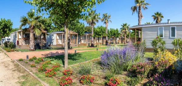 Mobile homes with porches among trees and colorful flower beds; clear blue sky at El Pinar