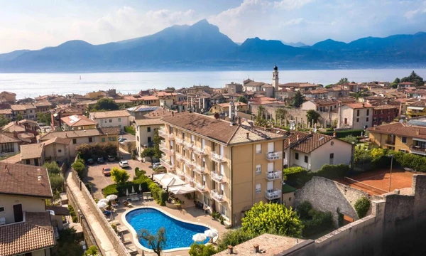 Hotel stands beside a swimming pool surrounded by trees and houses, with a mountainous backdrop at Hotel Romeo
