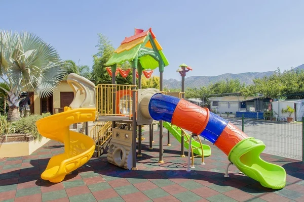 Colorful playground equipment with slides and tunnels on a rubber matting surface in an outdoor setting with mountains at Armanello