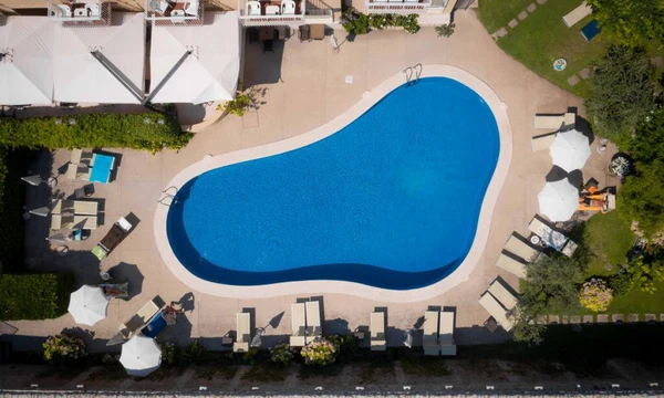 Swimming pool reflecting blue water, surrounded by sun loungers and umbrellas, situated in a landscaped area at Hotel Romeo
