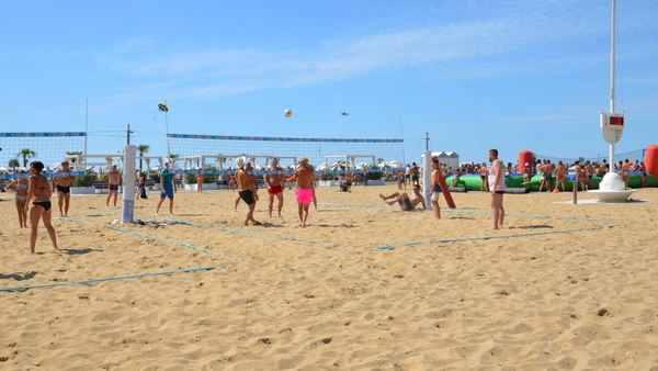 People playing volleyball on a sandy beach, surrounded by sunbathers and inflatable structures at Savoy Beach Hotel & Thermal Spa