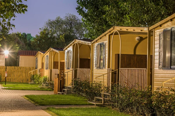 Row of wooden cabins with steps, illuminated by a streetlight, surrounded by trees and greenery at hu Venezia Camping in Town