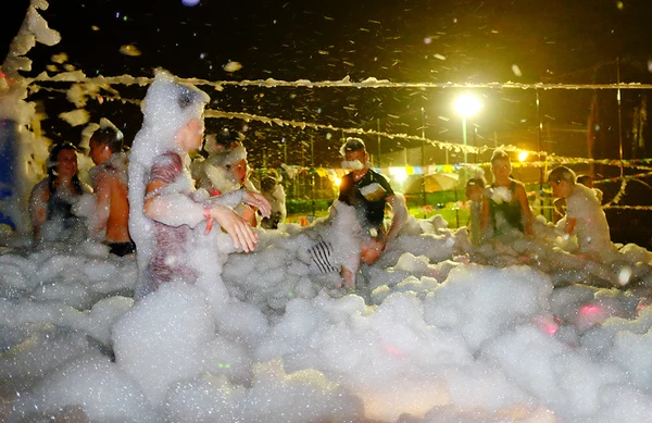 People play in soap foam bubbles at night under strings of lights at El Pinar
