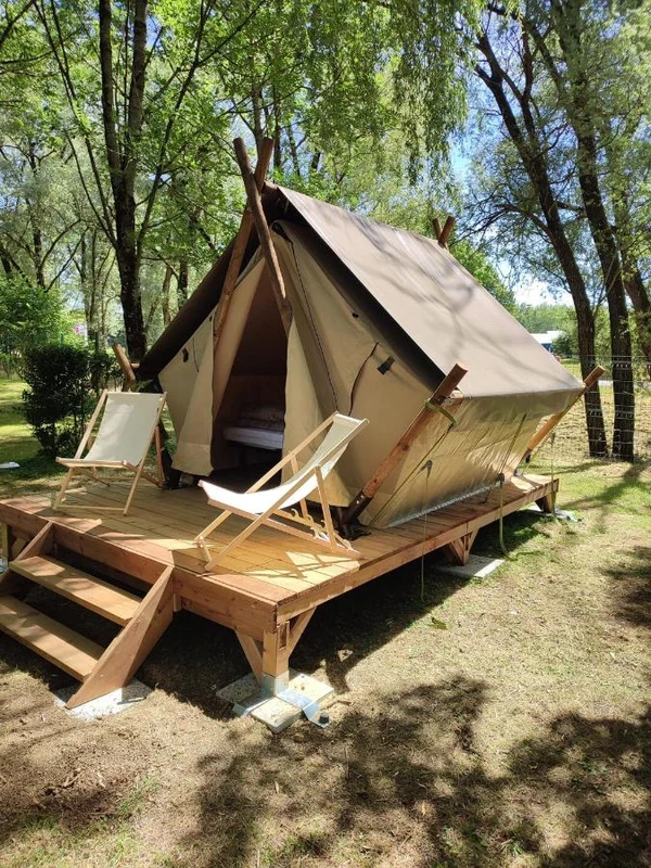 Canvas tent with wooden platform, two empty lounge chairs, set in a wooded campsite at Seasonova Du Chêne