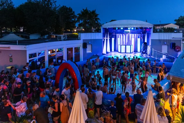 People dancing and socializing at a vibrant, outdoor, poolside party with lit stage in the background at Marvilla Parks Club Le Napoléon
