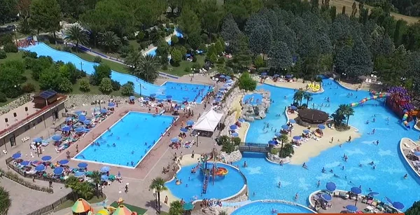 Several pools with slides and people swimming, surrounded by trees, umbrellas, and sun loungers at Centro Vacanze Verde Azzurro