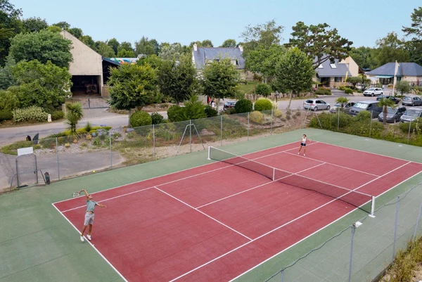 Two people playing tennis on a fenced court, surrounded by greenery and parked cars at Les 2 Fontaines
