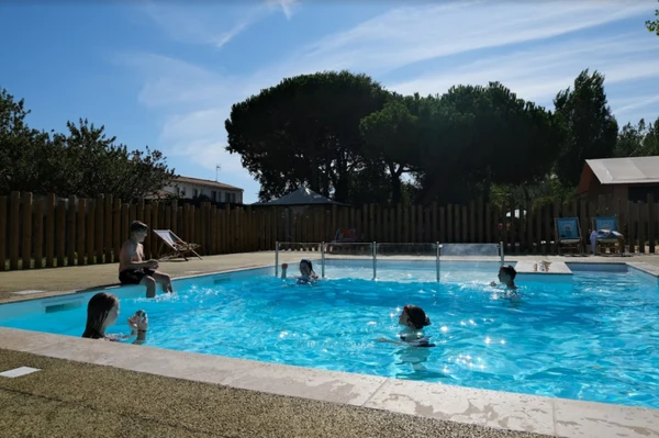 Children swimming and playing in a small outdoor pool surrounded by trees and lounge chairs at Seasonova Ile de Ré