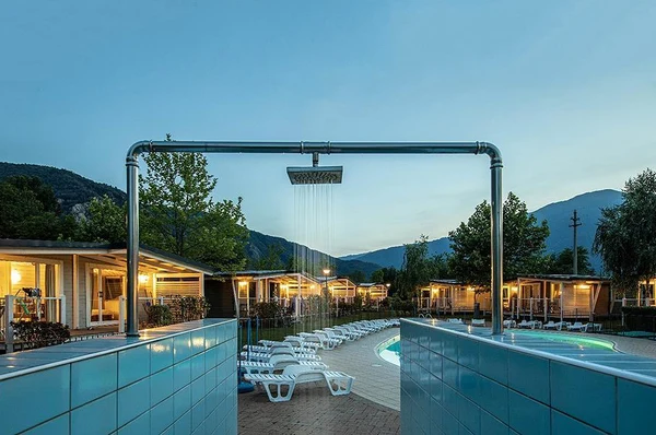 Outdoor shower running beside a pool surrounded by lounge chairs, cabins, and mountains at Glamping II Borgo delle Arti
