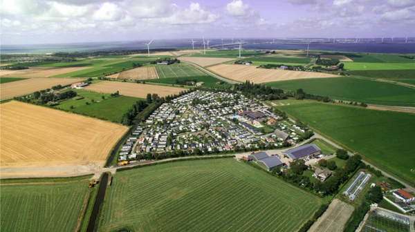 Aerial view of a large campsite situated among fields, with wind turbines in the distant background at Camping de Molenhoek