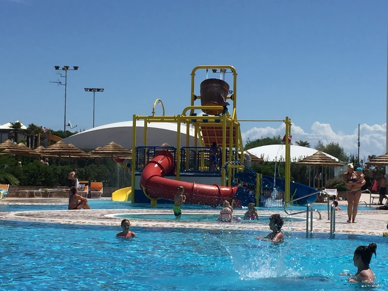 Children playing on water slides and in a pool, surrounded by greenery and straw umbrellas at Internazionale