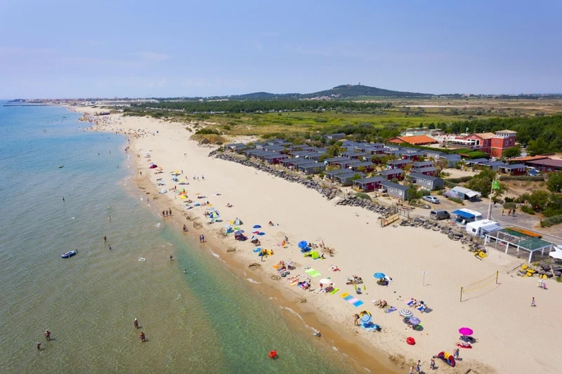 Beachgoers relaxing and swimming on a sandy beach lined with umbrellas and near rows of beach houses at Les Méditerranées Beach Garden