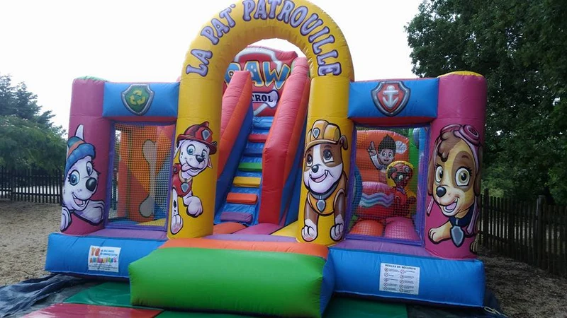 Inflatable bouncy castle with Paw Patrol characters, featuring slides and enclosed play areas, in an outdoor, fenced park setting at l'Évasion