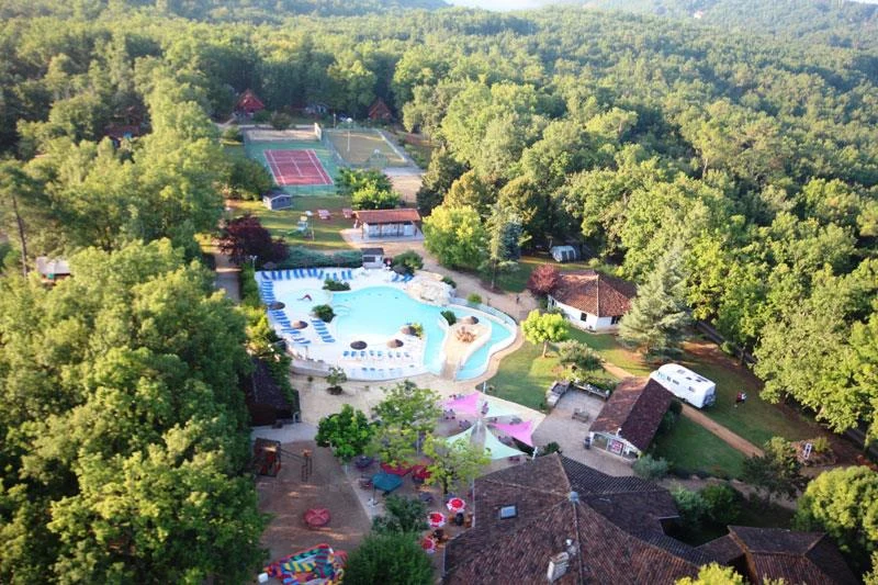 Aerial view of a swimming pool surrounded by chairs, nearby buildings, and sports courts in a forested area at l'Évasion