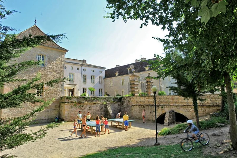 Children playing table tennis near a historic stone building with a cyclist passing by, surrounded by trees at Château de l'Epervière