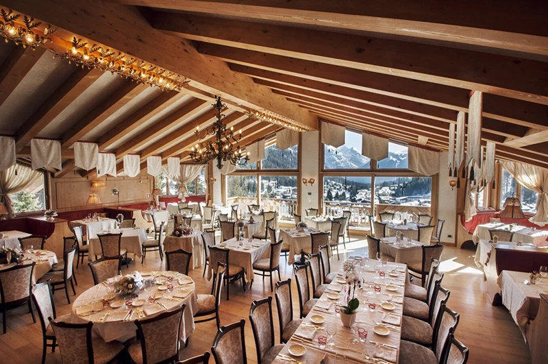 Dining tables arranged elegantly, adorned with white tablecloths, set in a cozy restaurant with large windows framing snowy mountains at Cristal Palace Resort